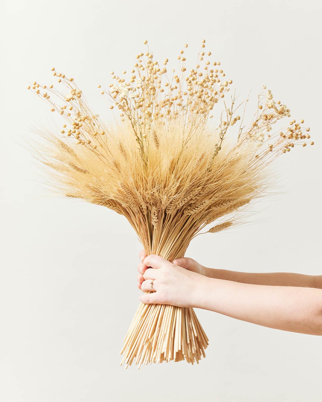 Studio image of hands holding the medium harvest arrangement on a cream/grey background