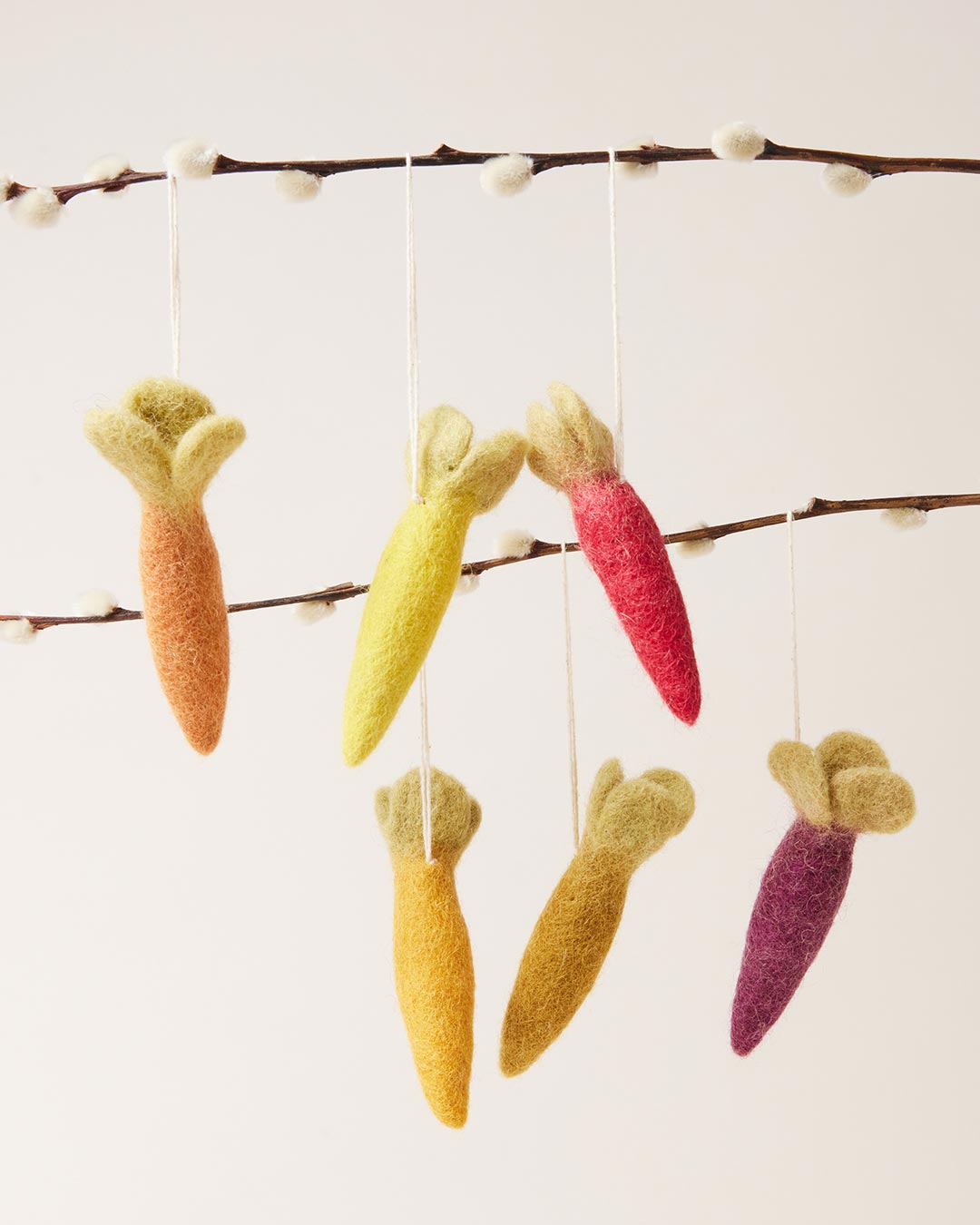Farmhouse Pottery Felted Carrot Spring Ornaments hanging on a branch with a white background.